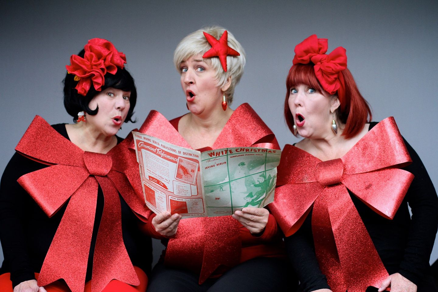 Three women dressed in big red bows singing